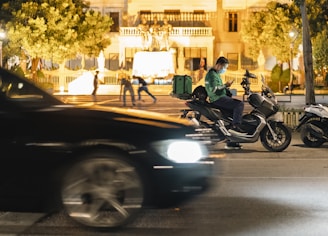 a man riding a motorcycle down a street next to a car