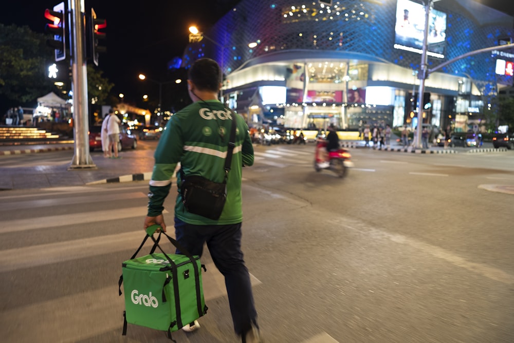 a man walking across a street holding a green bag