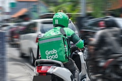 A friendly Gojek driver assisting a customer with a smile in a busy urban street.
