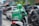 A GrabFood delivery person wearing a green uniform and helmet is riding a motorbike in a busy urban street amid traffic. The rider has a large insulated delivery bag on their back that features the GrabFood logo.