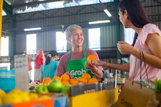 a woman in a green apron standing in front of a table filled with oranges