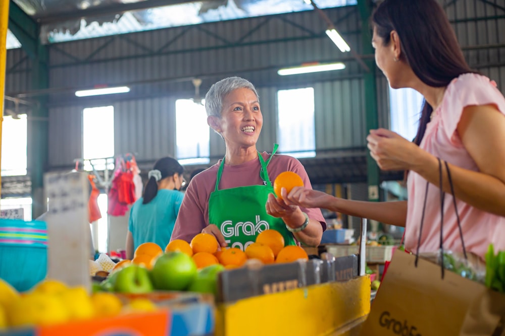 a woman in a green apron standing in front of a table filled with oranges