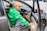 A person wearing a cap and a green jacket with the Grab logo is seated in a car, holding onto the door as it is open. The focus is on the interior and the person, with parts of the car like the dashboard, steering wheel, and side mirror visible.