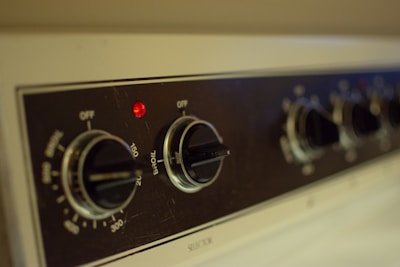 Close-up view of a kitchen appliance control panel featuring several black knobs with temperature settings visible and a small red indicator light. The panel has labels for various cooking modes such as 'Broil' and temperature increments, with the design emphasizing functionality.