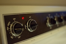 Close-up view of a kitchen appliance control panel featuring several black knobs with temperature settings visible and a small red indicator light. The panel has labels for various cooking modes such as 'Broil' and temperature increments, with the design emphasizing functionality.