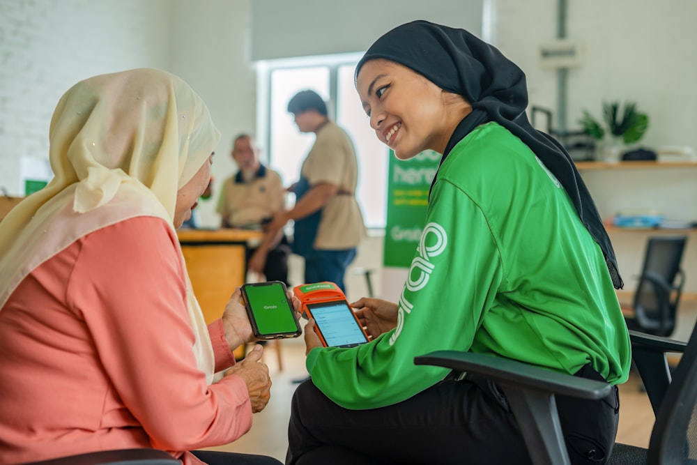 a woman in a hijab is showing another woman a cell phone