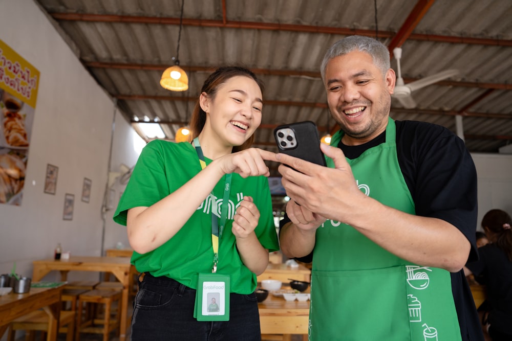 a man and woman in green aprons looking at a cell phone