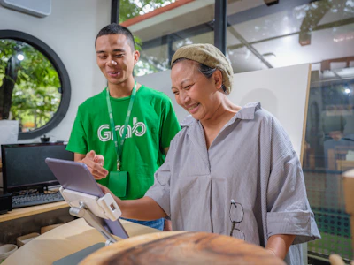 An operator assisting a caregiver using a tablet, with a bright office backdrop.