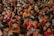A large group of children of various ages are gathered closely together, with many looking directly at the camera. Some children are smiling, others are making playful hand gestures, and they are dressed in colorful clothing.