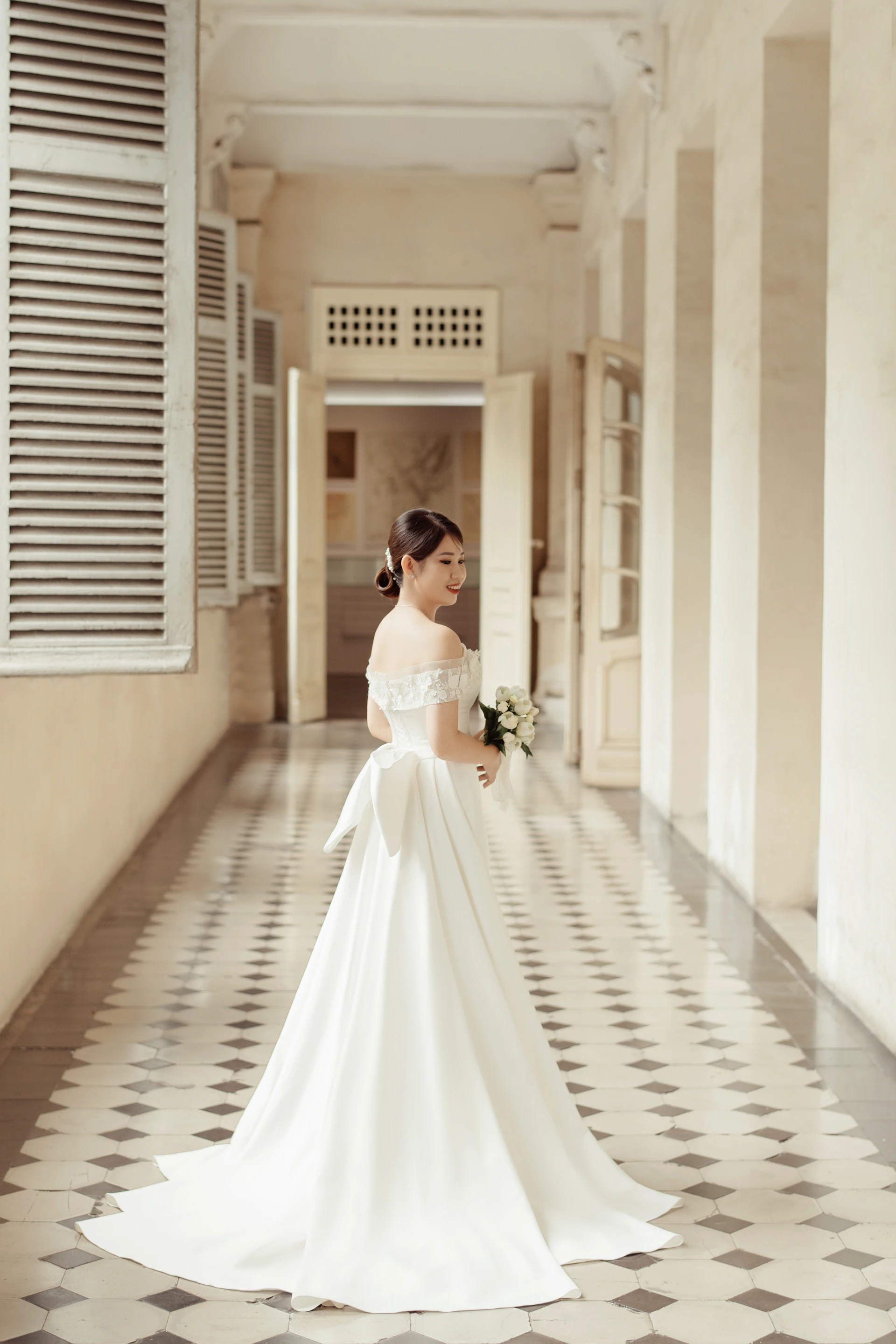 A bride in an elegant long train wedding dress standing gracefully against a soft white background, embodying timeless beauty.