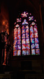 A craftsman carefully restoring a colorful stained glass window in a sunlit workshop.