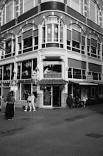 A multi-story building with intricate architectural details, featuring large windows and a decorative facade. The ground floor houses a restaurant called 'Oriental City' with signs in English and Chinese. Several people are standing outside, and a few tables are occupied with diners on the sidewalk.