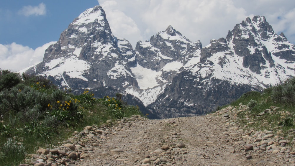 a dirt road in front of a snow covered mountain