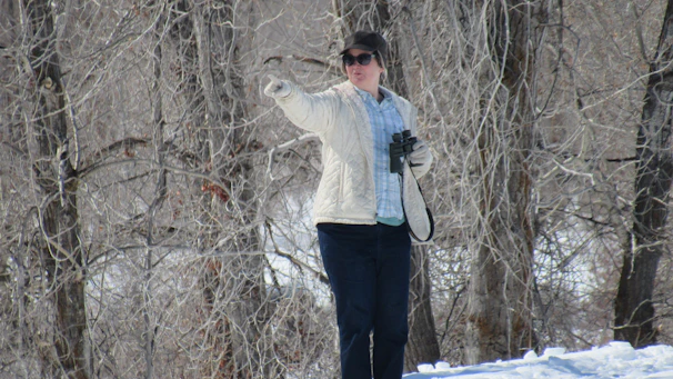 Instructor demonstrating avalanche beacon use to attentive winter sports enthusiasts in a snowy forest clearing.