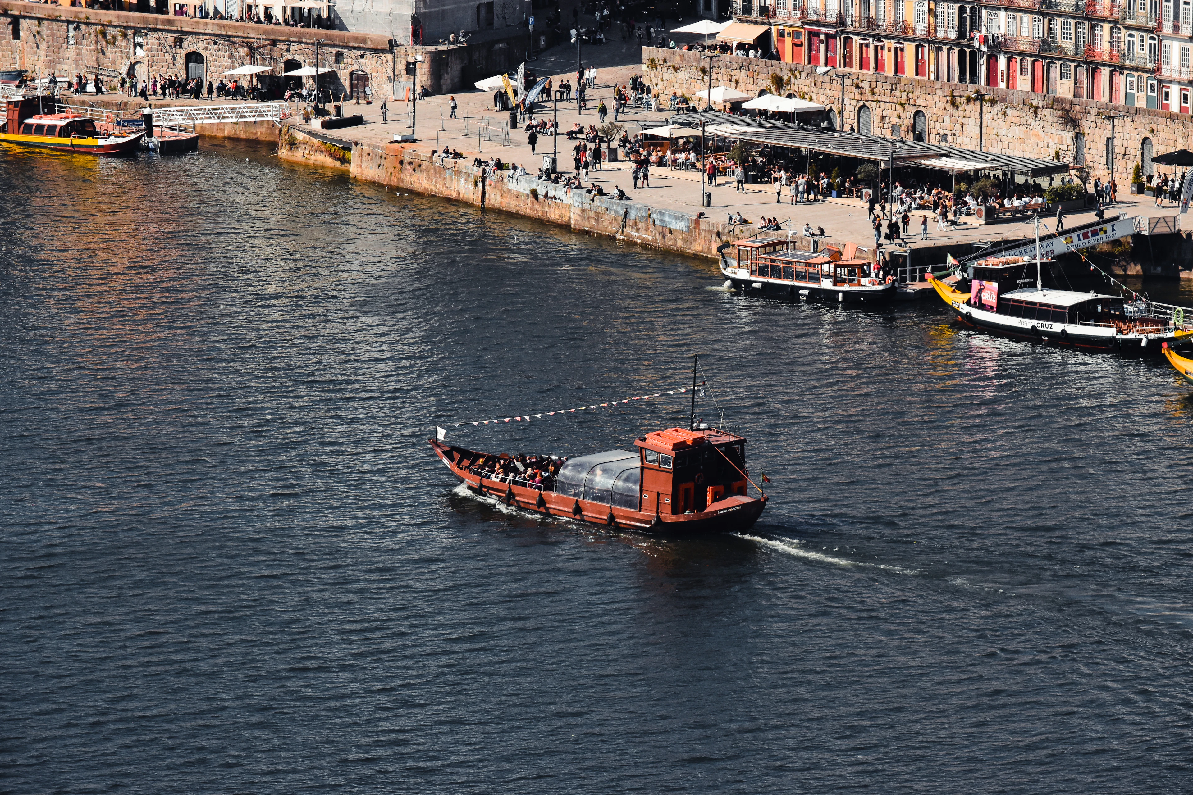 A traditional rabelo boat crossing the Douro River in front of Porto's riverside Ribeira district.