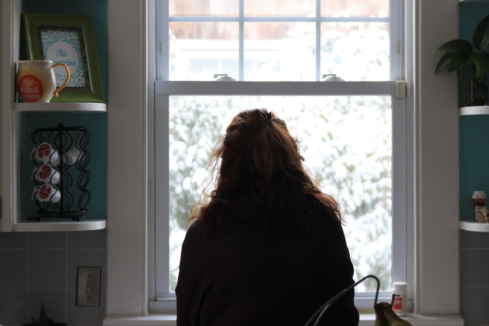 a woman sitting in front of a kitchen window