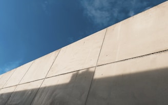 Workers laying concrete blocks to build a sturdy wall under a clear sky.