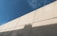 A large concrete wall is visible under a clear blue sky. The wall is segmented into panels and casts a shadow on its surface.