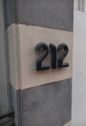 Metallic numbers 212 are mounted on a light-colored wall, framed by darker vertical stripes. The numbers have a three-dimensional, rounded design.