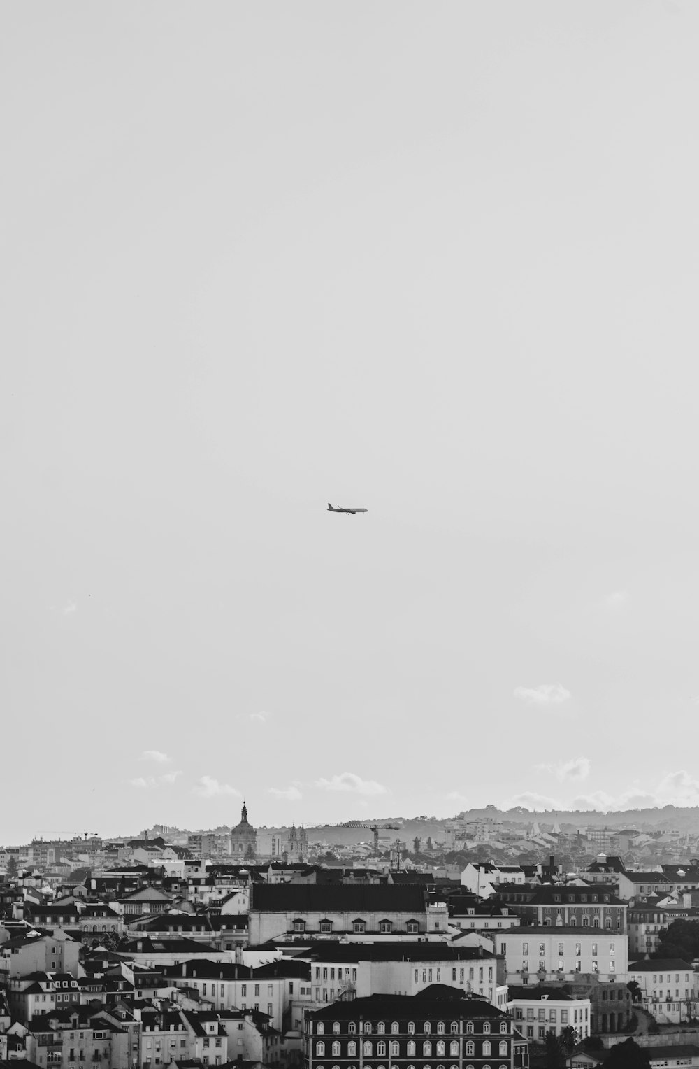 a black and white photo of a plane flying over a city