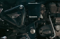 A close-up view of the side of a motorcycle engine, showcasing the intricate mechanical parts and branding details such as 'Bullet 350' and 'hermano'. The image focuses on the metallic and polished components, highlighting the craftsmanship of the motorcycle.