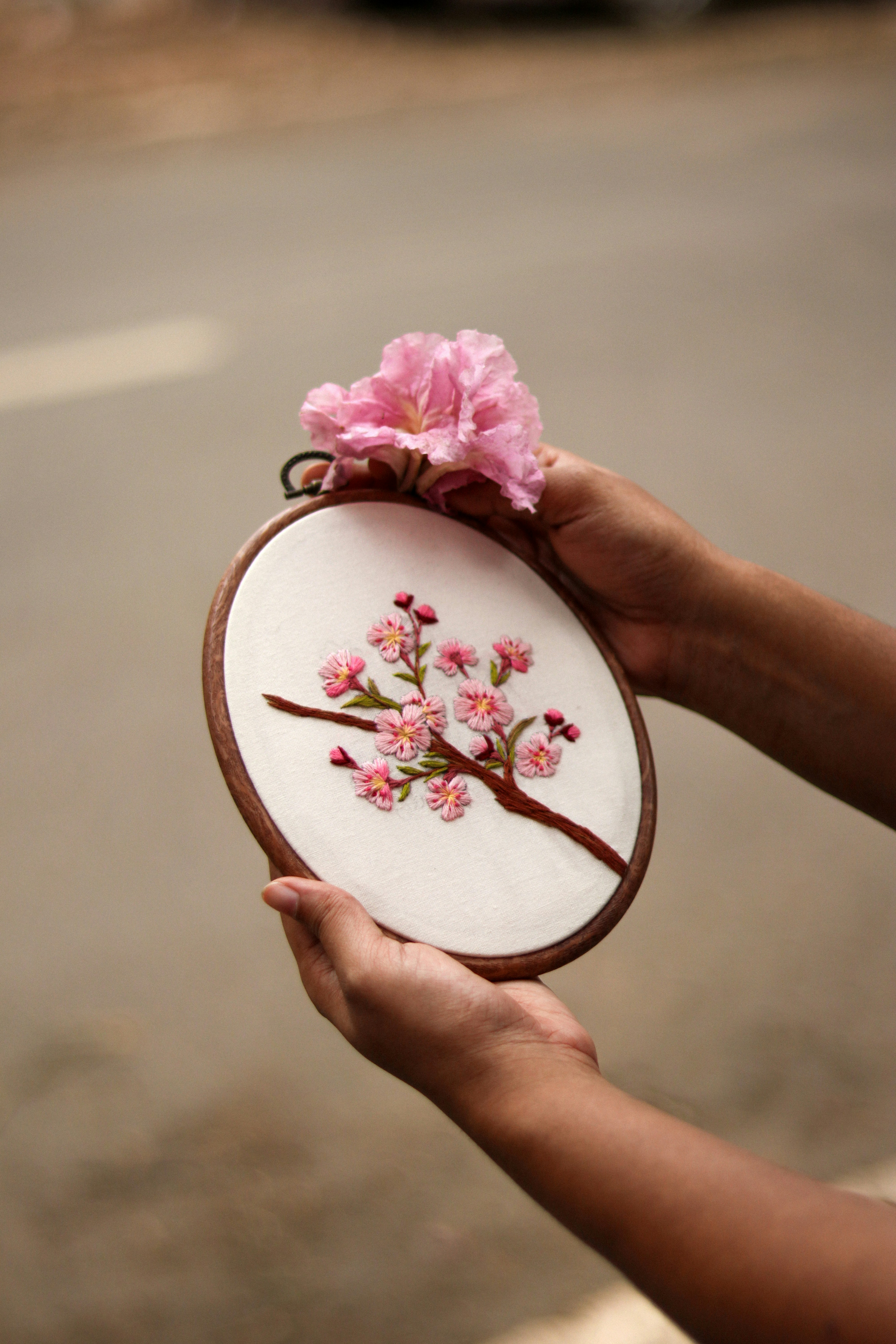a person holding a small embroidered object with a pink flower on it
