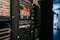 A data center with rows of servers in racks, featuring various network and power connections. Orange and black cables are visible, alongside multiple server units with indicator lights. The environment appears organized with subdued lighting.