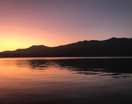 A serene sunset casting golden light over a quiet mountain lake, reflecting the sky's warm hues.