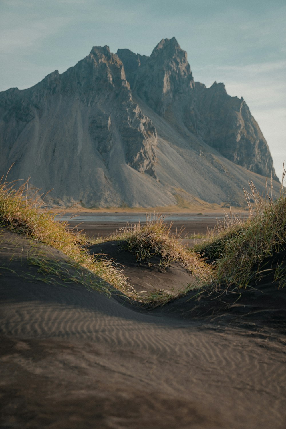 uma cordilheira ao longe com grama crescendo da areia