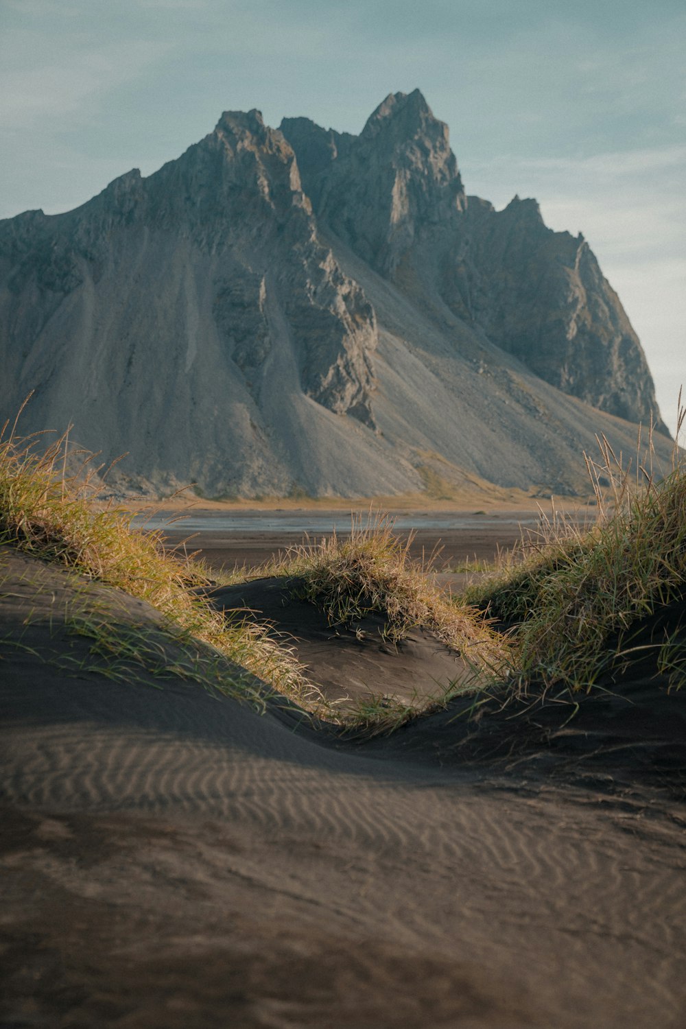 a mountain range in the distance with grass growing out of the sand