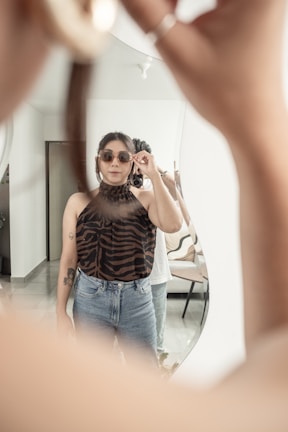 Woman adjusting cat-eye glasses in front of a mirror with warm lighting.