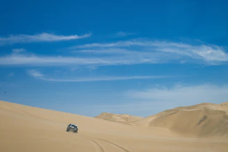 Experienced driver guiding a 4x4 vehicle through the dunes under a clear sky.