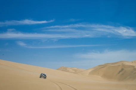Experienced driver guiding a 4x4 vehicle through the dunes under a clear sky.