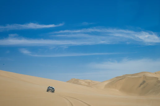 A rugged Liwa Wind ATV kicking up sand as it races across golden Liwa Desert dunes under a clear blue sky.