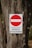 A weathered tree trunk serves as the background for a metal sign displaying a red circle with a white horizontal bar inside it. Beneath the circle, the text reads 'PROPRIETA' PRIVATA DIVIETO DI ACCESSO' indicating private property and no entry.