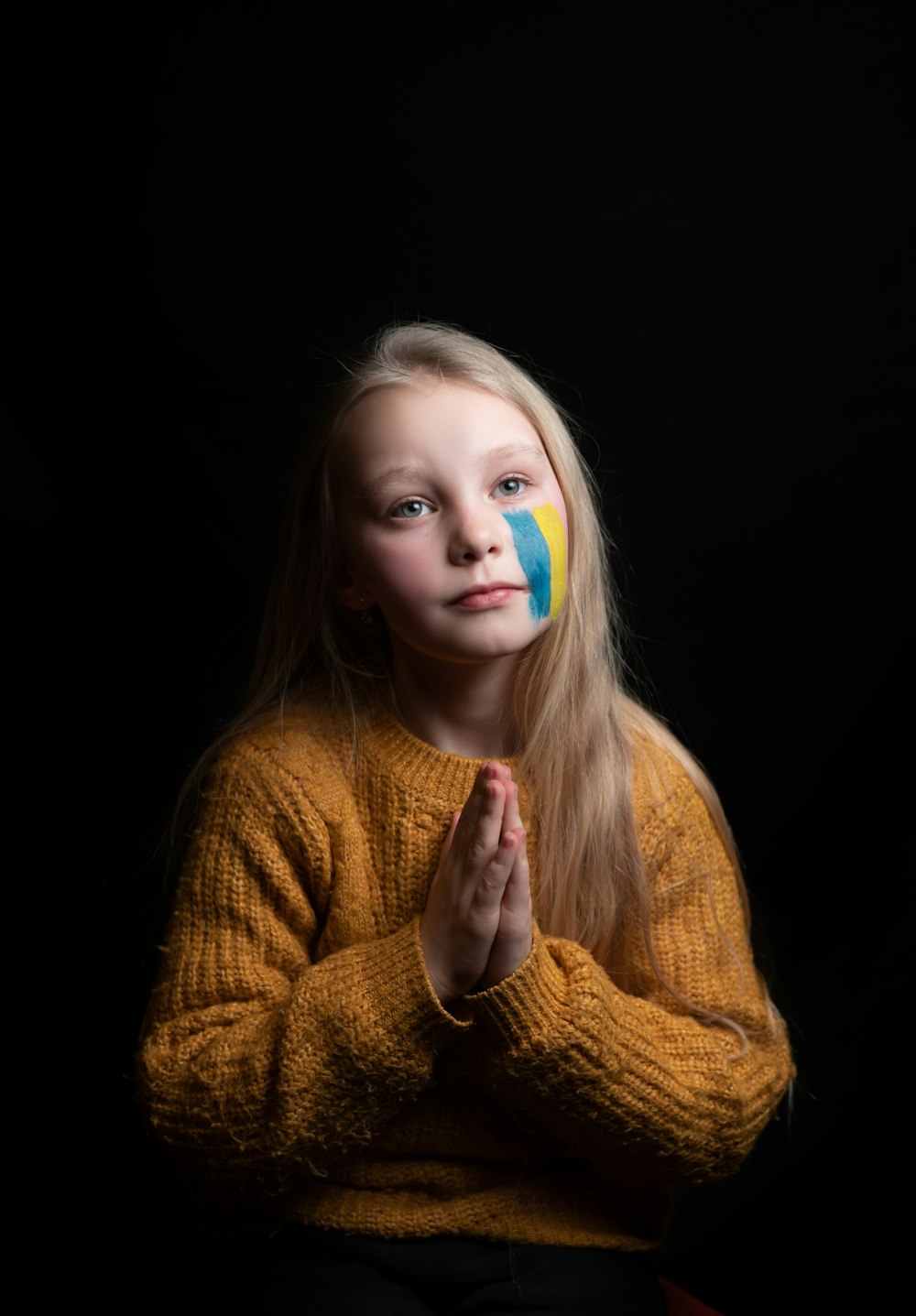 a little girl with a painted face sitting in front of a black background