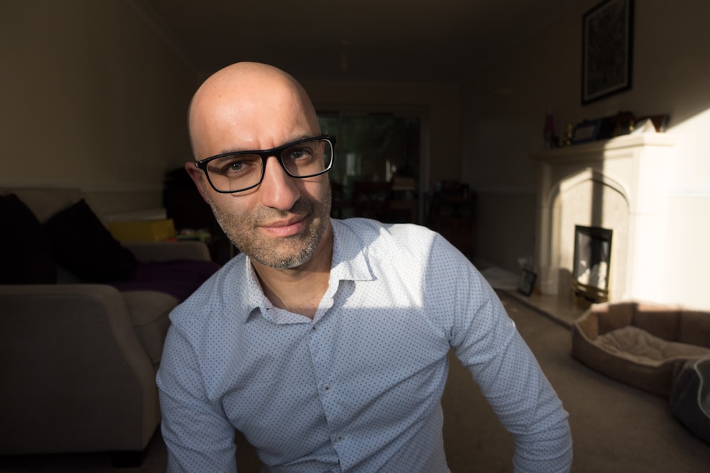 a bald man wearing glasses standing in a living room