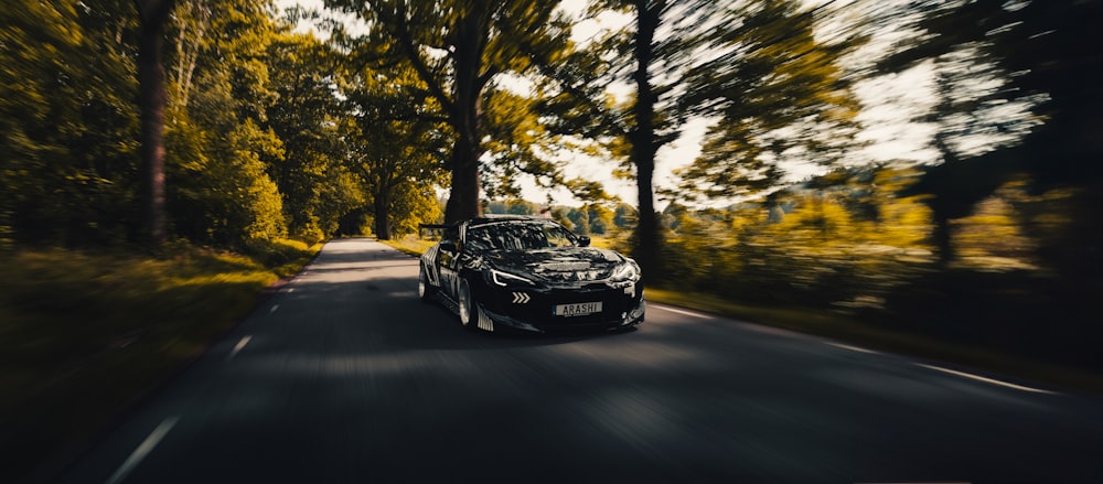 a black sports car driving down a tree lined road