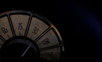 A close-up view of a vintage radio dial featuring numbers in increments of fifteen, from 65 to 120. The dial is set within a dark, textured background, and the numbers are highlighted in a golden hue.