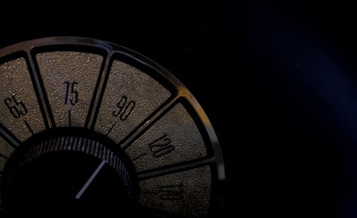 A close-up view of a vintage radio dial featuring numbers in increments of fifteen, from 65 to 120. The dial is set within a dark, textured background, and the numbers are highlighted in a golden hue.