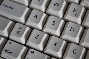 Close-up view of a computer keyboard featuring white keys with black lettering. The keys displayed include letters like W, A, S, D, and special characters such as < and >.