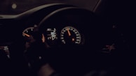 A dimly lit car dashboard with illuminated speedometers and gauges indicating a speed of 80 km/h. The steering wheel is visible, suggesting the driver's perspective.