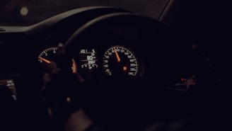 A dimly lit car dashboard with illuminated speedometers and gauges indicating a speed of 80 km/h. The steering wheel is visible, suggesting the driver's perspective.