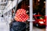 A person wearing a red bucket hat with white maple leaf patterns stands under scaffolding at night. In the background, there is a brightly lit street with a red car passing by.
