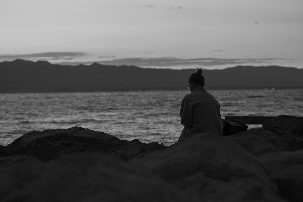 a person sitting on a rock near the water