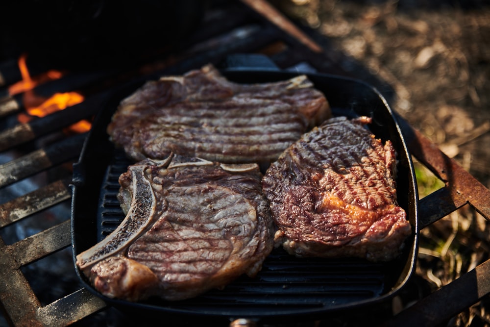 steaks are cooking on a grill in the woods