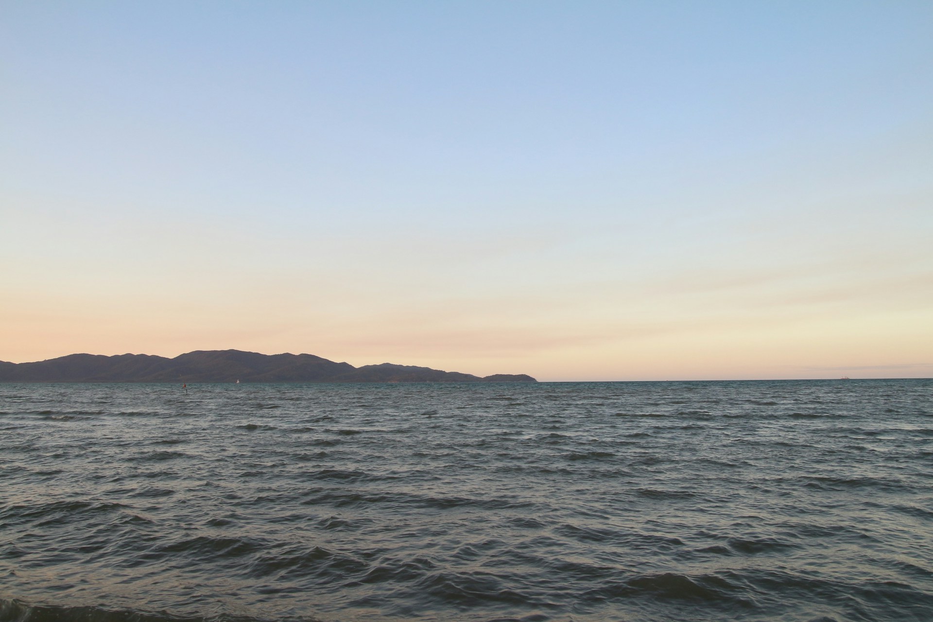 A peaceful horizon at dawn where the calm sea meets the pastel colors of the rising sun, with gentle ripples on the water.