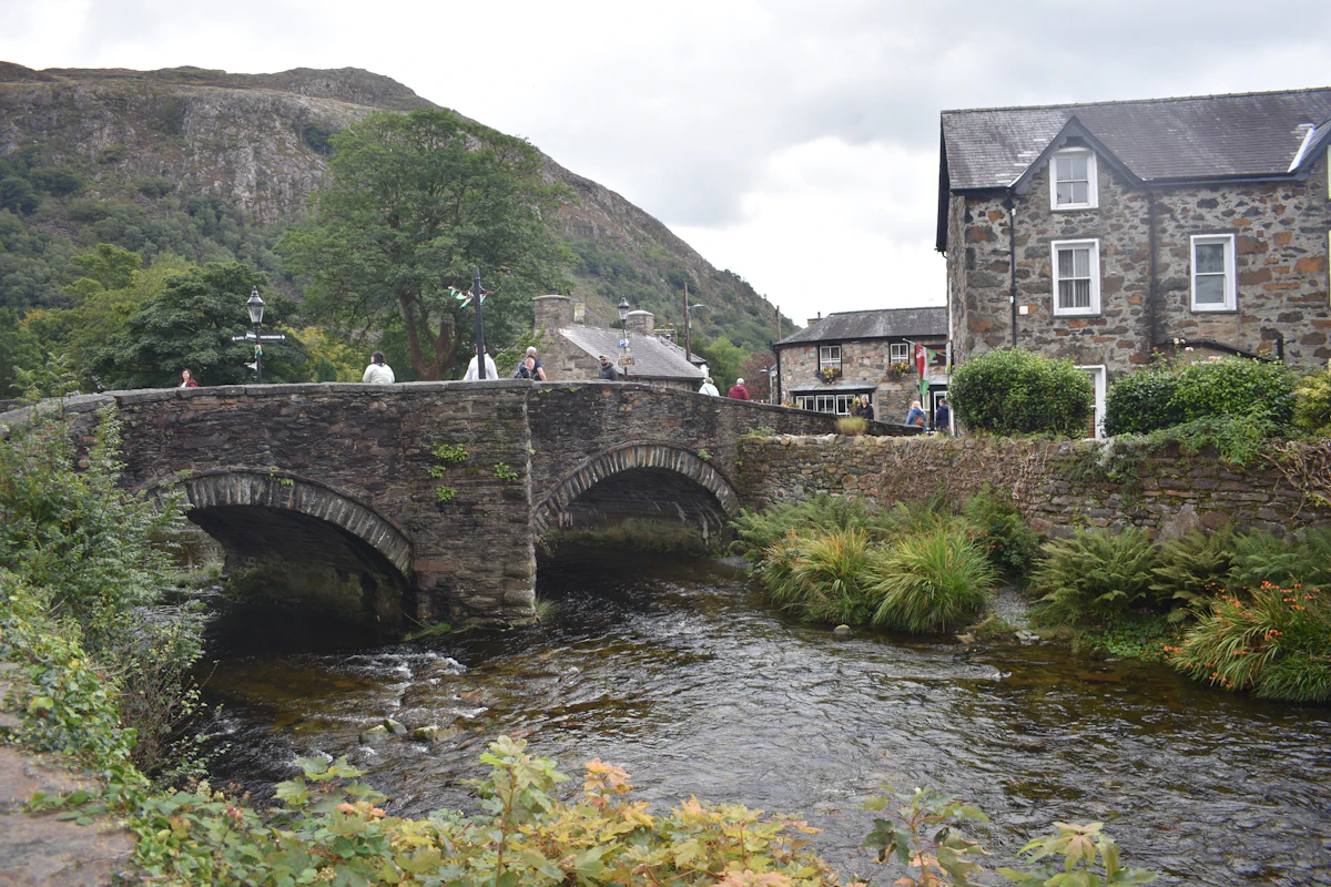 A stone bridge over the river in Beddgelert, with slate houses and a wooded hillside