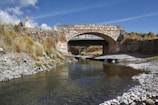 Stone bridge arching over a gently flowing stream in a peaceful alpine valley