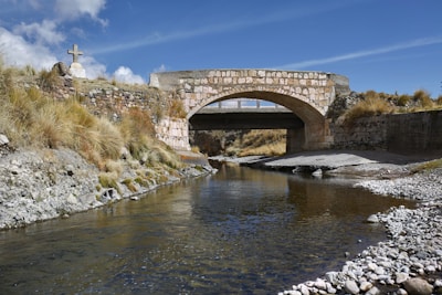Stone bridge arching over a gently flowing stream in a peaceful alpine valley